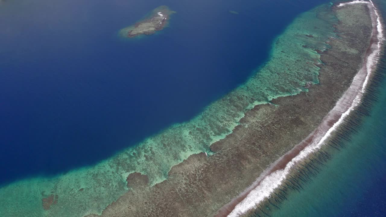 一架无人机飞越平静的海洋与珊瑚礁热带天堂岛的鸟瞰图。令人惊叹的自然景观，蓝色的泻湖和太平洋。视频素材