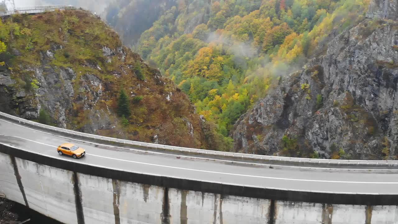 在雾蒙蒙的乡间小路上，汽车在桥上行驶。在秋天山路上的堤坝上骑车。航拍越野车通过风景秀丽的风景道。汽车旅行的概念。俯视图视频素材