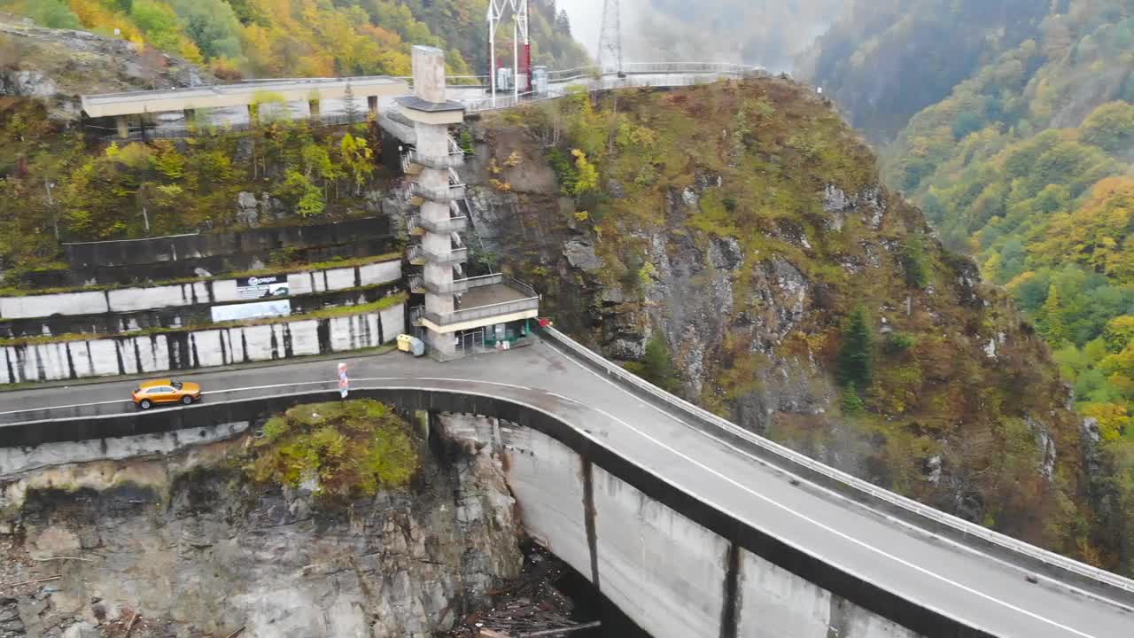 在雾蒙蒙的乡间小路上，汽车在桥上行驶。在秋天山路上的堤坝上骑车。航拍越野车通过风景秀丽的风景道。汽车旅行的概念。俯视图视频素材