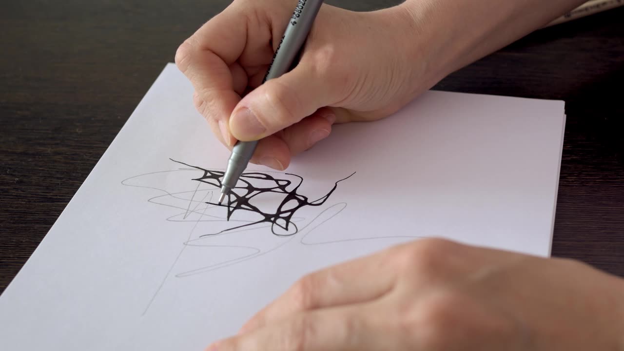 设计师用黑色记号笔在纸上作画。画家在纸上画素描。用手在纸上画线的线笔的特写。神经学和治疗视频素材画面1