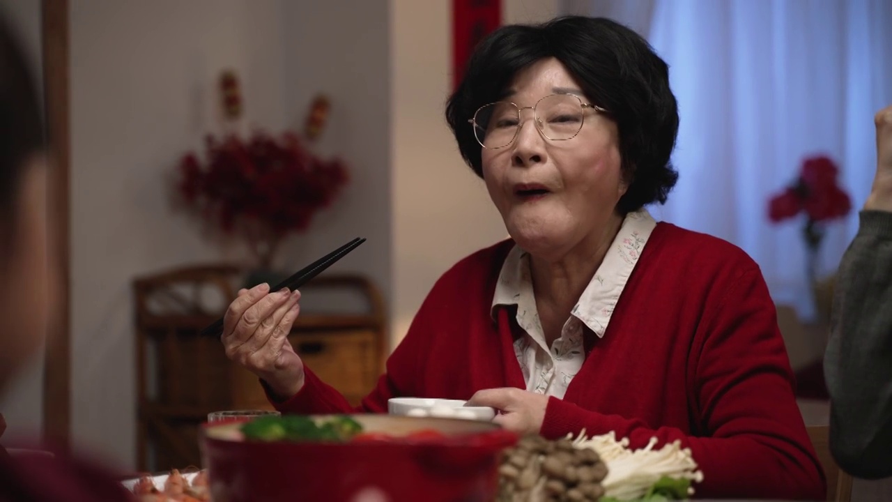 一位快乐的亚洲老妇人，红色的祖母，微笑着满意，与她的家人在中国新年除夕的餐桌上吃美味的食物视频素材画面1