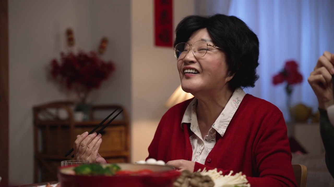 一位快乐的亚洲老妇人，红色的祖母，微笑着满意，与她的家人在中国新年除夕的餐桌上吃美味的食物视频素材画面2