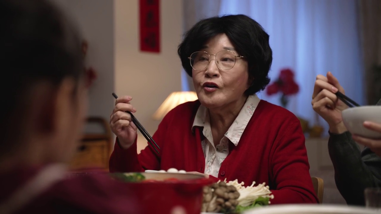 一位快乐的亚洲老妇人，红色的祖母，微笑着满意，与她的家人在中国新年除夕的餐桌上吃美味的食物视频素材画面3