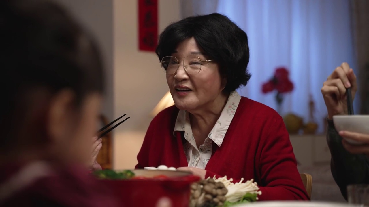 一位快乐的亚洲老妇人，红色的祖母，微笑着满意，与她的家人在中国新年除夕的餐桌上吃美味的食物视频素材画面4