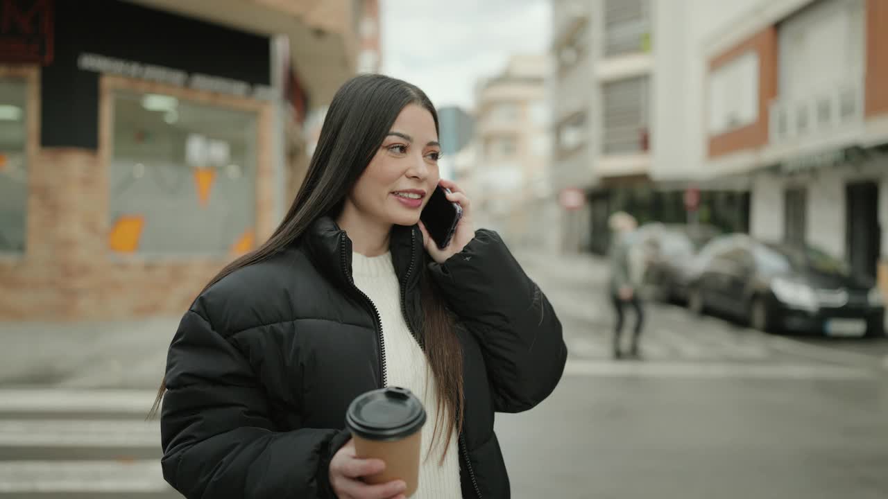 年轻的西班牙裔妇女在街上用智能手机打电话喝咖啡视频素材