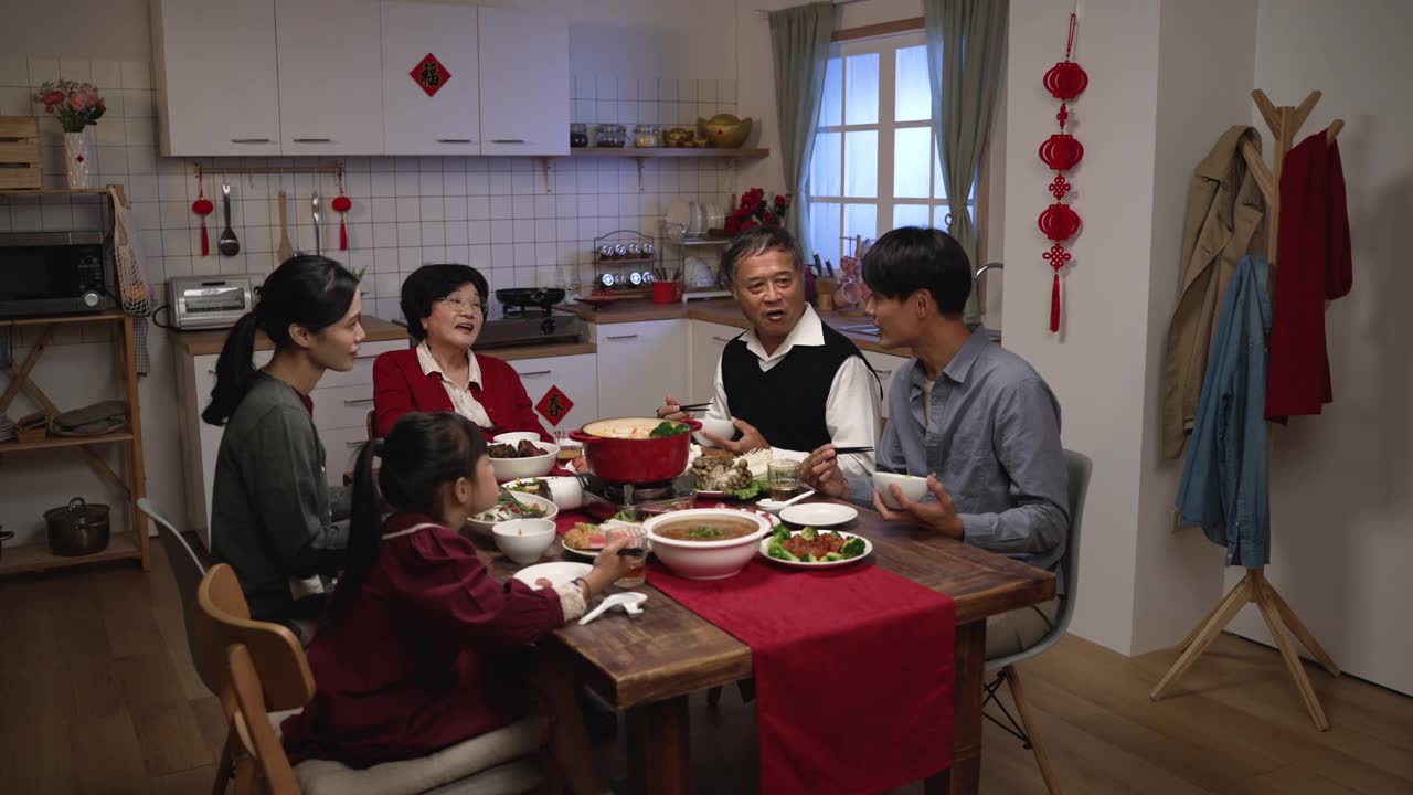 在家里吃年夜饭的时候，亚洲成年儿子微笑着拍着老父亲的肩膀，他们在餐桌上愉快地聊天视频素材画面1