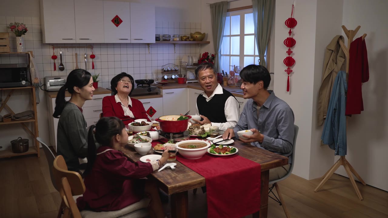 在家里吃年夜饭的时候，亚洲成年儿子微笑着拍着老父亲的肩膀，他们在餐桌上愉快地聊天视频素材画面2