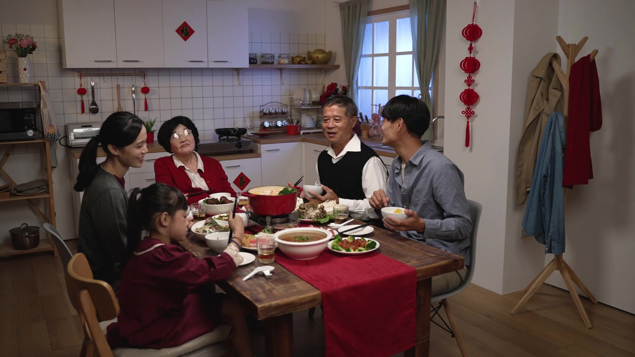 在家里吃年夜饭的时候，亚洲成年儿子微笑着拍着老父亲的肩膀，他们在餐桌上愉快地聊天视频素材画面3