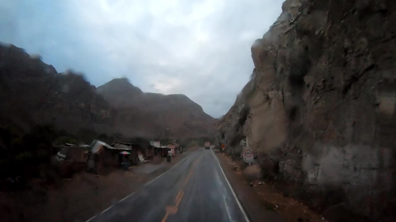 POV快速摄像机在路上的巴士旅行，而雨水淋湿了挡风玻璃，在日落时被山脉和蓝天包围视频素材