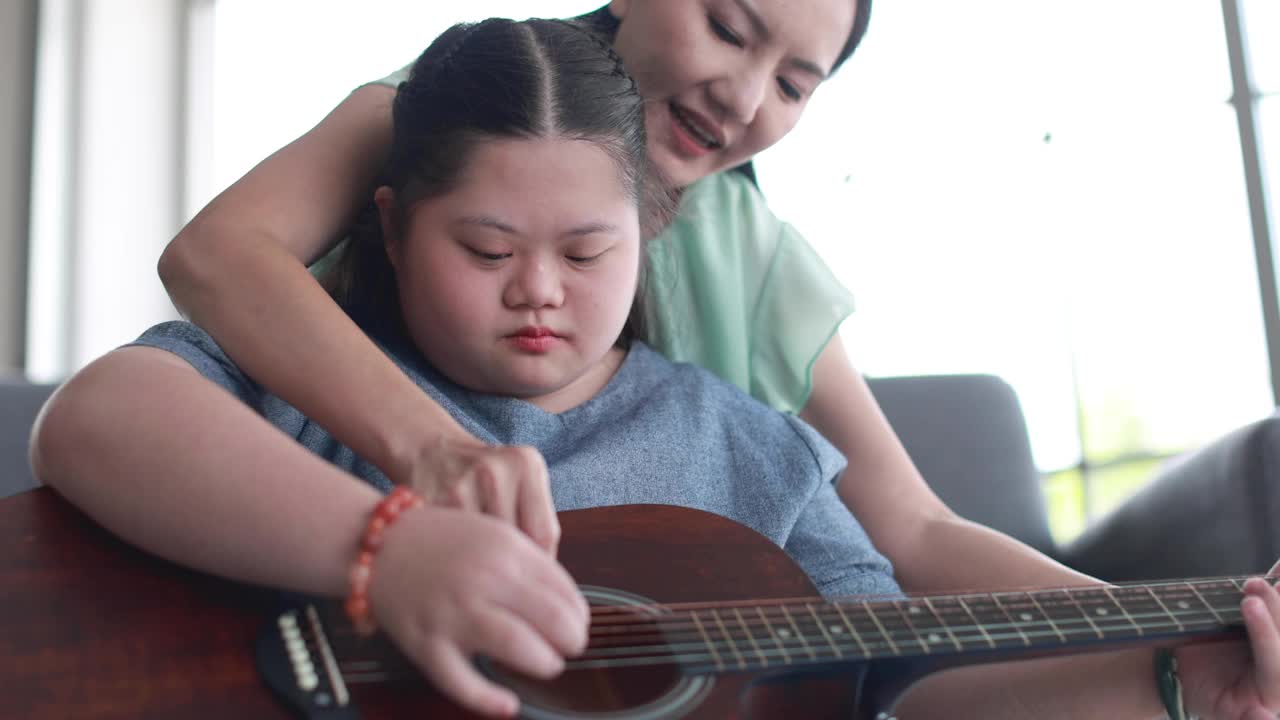 可爱的亚洲女人教孩子唐氏综合症演奏原声吉他，同时花时间在家里视频素材