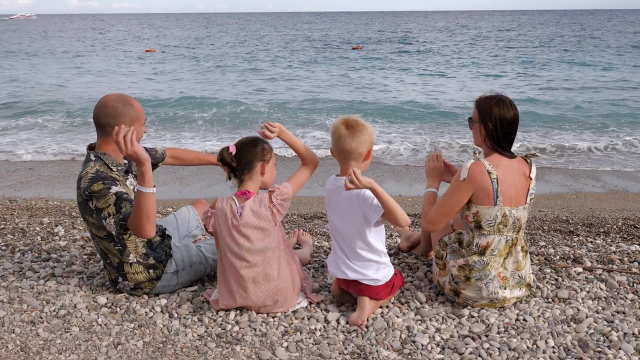 带着小孩的一家人坐在海边扔石头。视频素材画面1