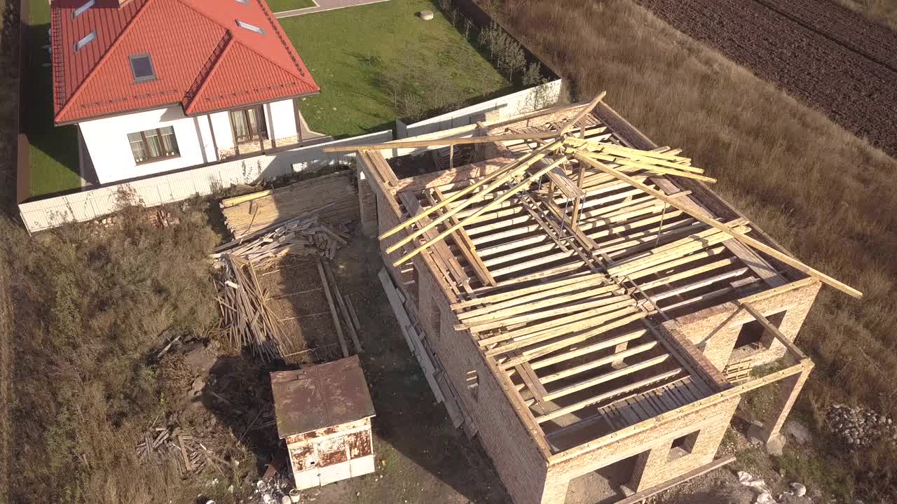 从上往下鸟瞰两间私人住宅，一间正在建造中，木质屋顶框架，另一间完成了红瓦屋顶。视频素材