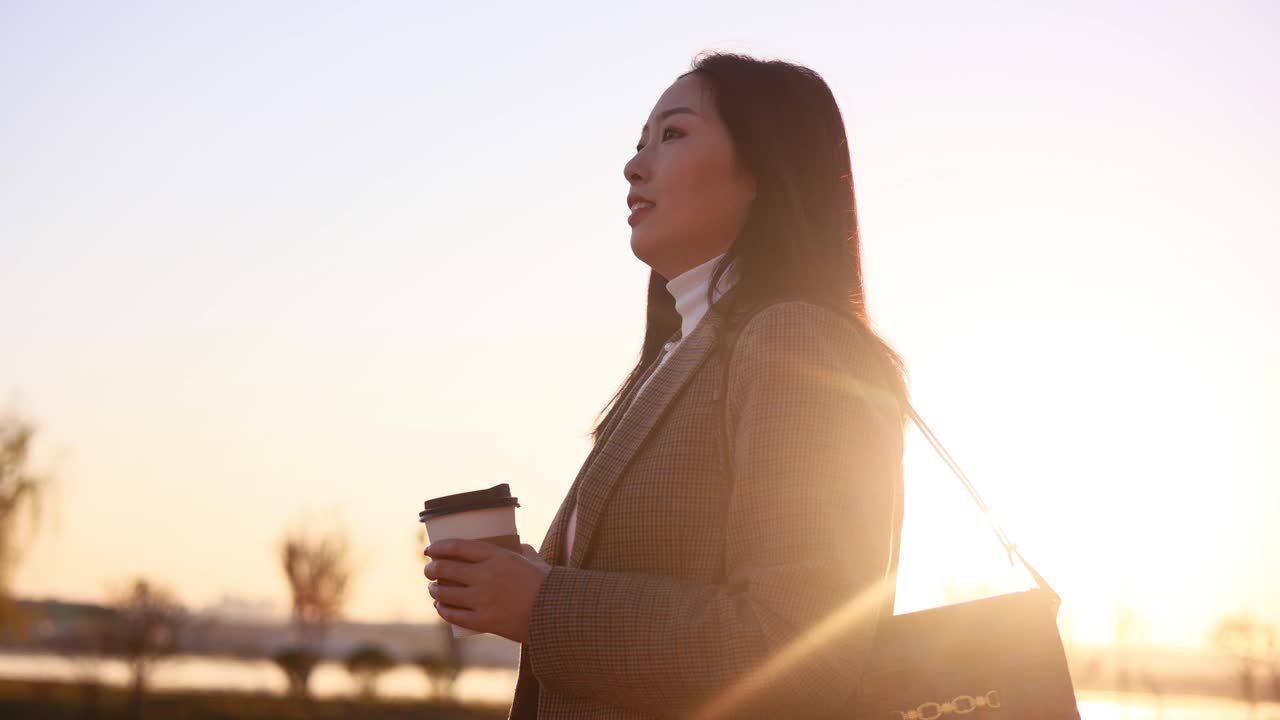 年轻女子拿着咖啡杯漫步在城市的早晨视频素材