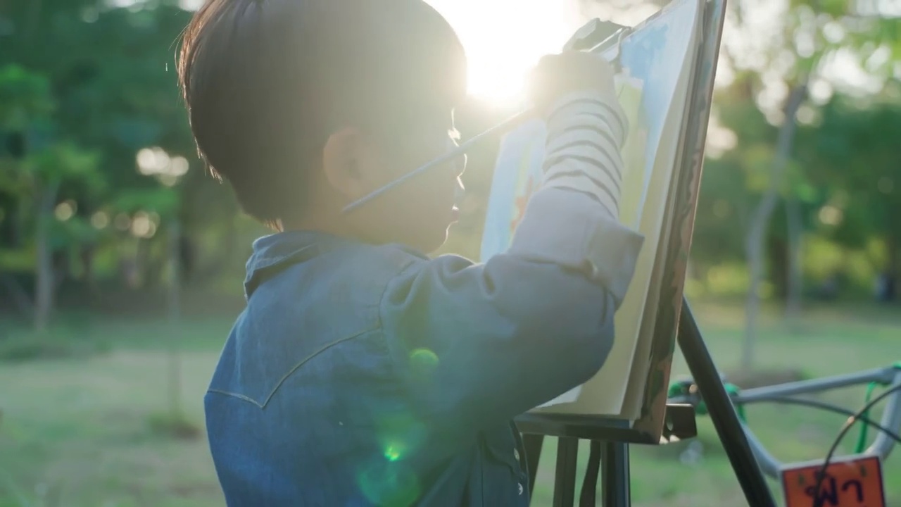 这个男孩用水彩画和画笔在村庄、公园里画画。视频素材画面4