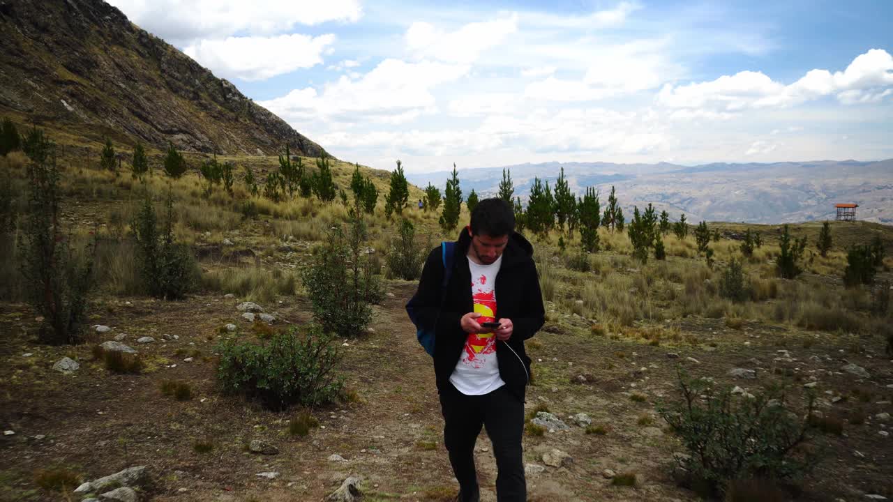 一名男子在秘鲁瓦拉兹高地的灌木丛和植被中徒步穿越山脉，看着他的手机视频素材