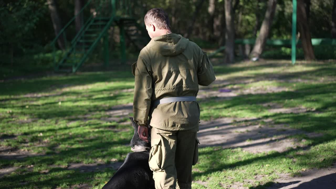 跟踪拍摄了一个白人男子和德国牧羊犬在阳光明媚的日子里在户外行走，专业的狗狗专家正在快步旋转。狗跟随训练师的动作。服从训练。视频素材