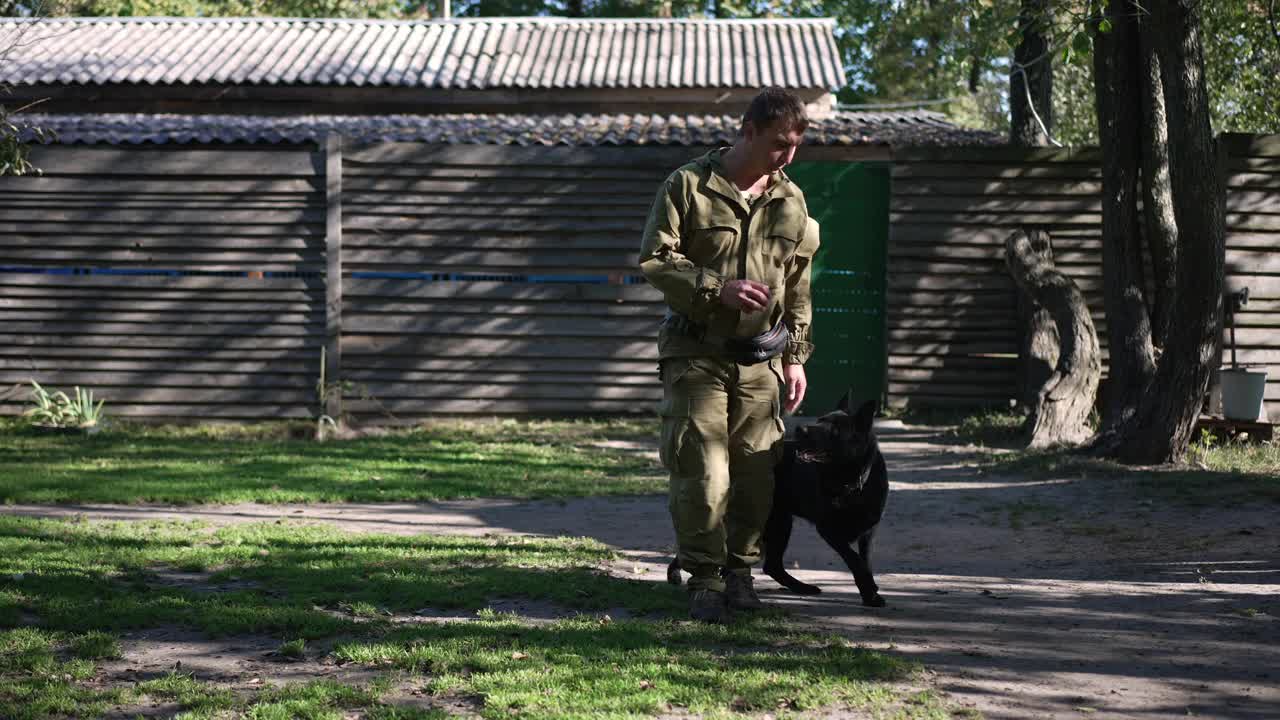 好奇的德国牧羊犬跟随严肃的犬科专家慢动作走路，手里拿着球。顺从的黑狗跟随专业的白人男子训练宠物户外。视频素材