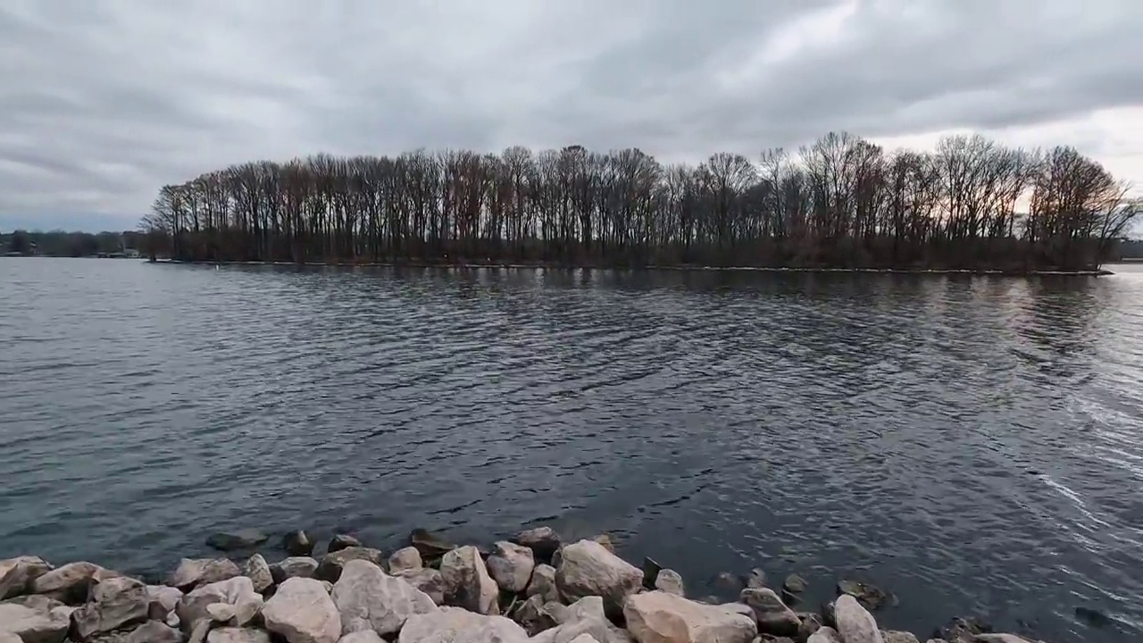 岛上冬天光秃秃的树木的剪影。遥望海军蓝的冬季湖水在地平线上汇合。阴暗的,喜怒无常的天空。视频素材