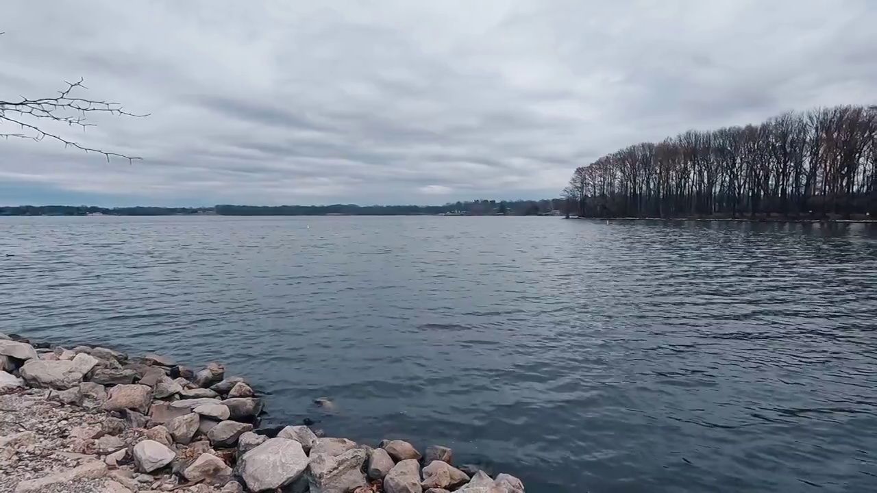 岛上冬天光秃秃的树木的剪影。遥望海军蓝的冬季湖水在地平线上汇合。阴暗的,喜怒无常的天空。视频素材