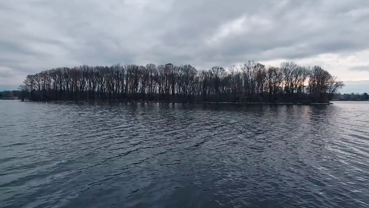 岛上冬天光秃秃的树木的剪影。遥望海军蓝的冬季湖水在地平线上汇合。阴暗的,喜怒无常的天空。视频素材