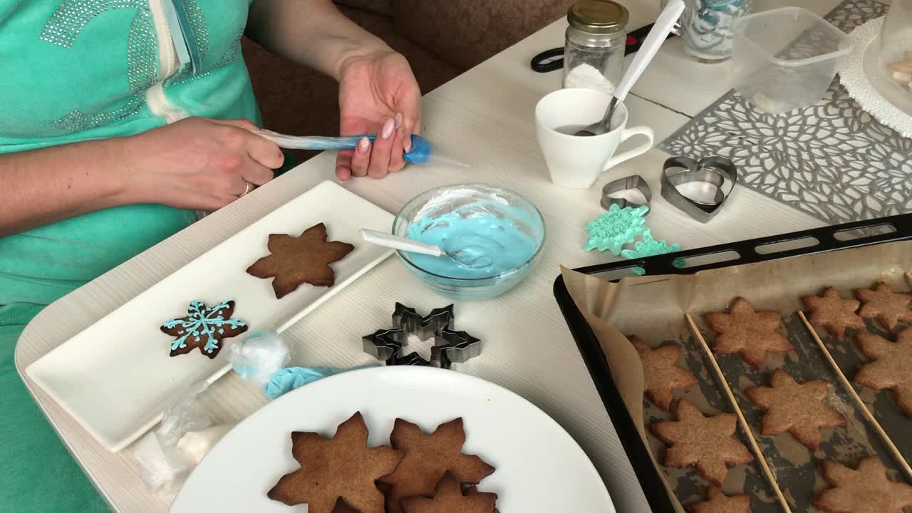 一位女士在糕点袋里装满糖霜来装饰姜饼。旁边是雪花形状的姜饼。总体规划。视频素材