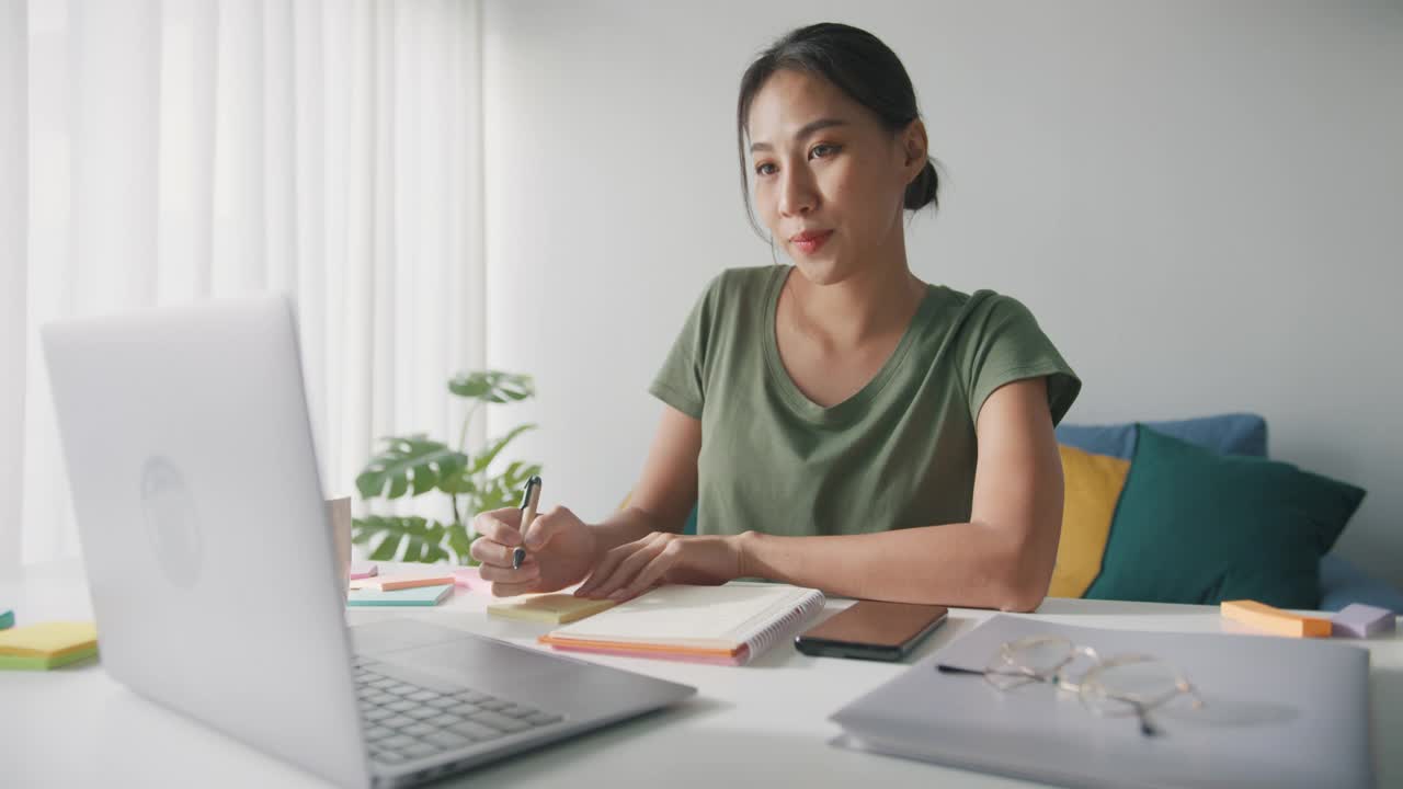 亚洲商务女性，穿着休闲服装，在家中客厅用笔记本电脑工作。视频素材