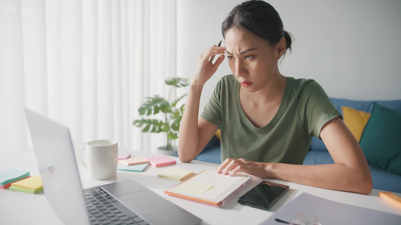 疲倦的年轻亚洲商业妇女在休闲工作笔记本电脑在客厅在家里。视频素材