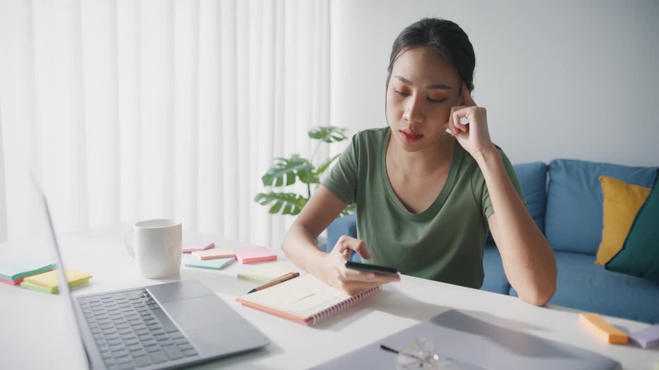 疲倦的年轻亚洲商业妇女在休闲使用电话在客厅在家里。视频素材