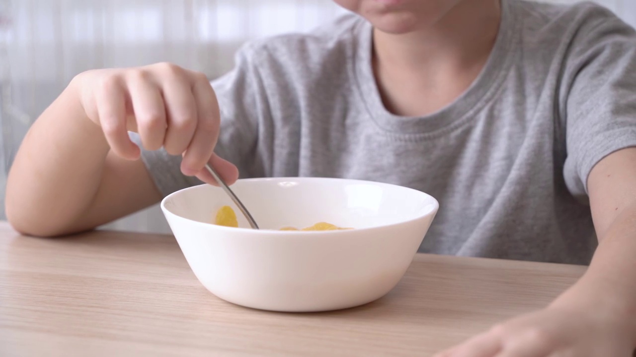 心满意足的小男孩早餐吃麦片加牛奶。视频素材