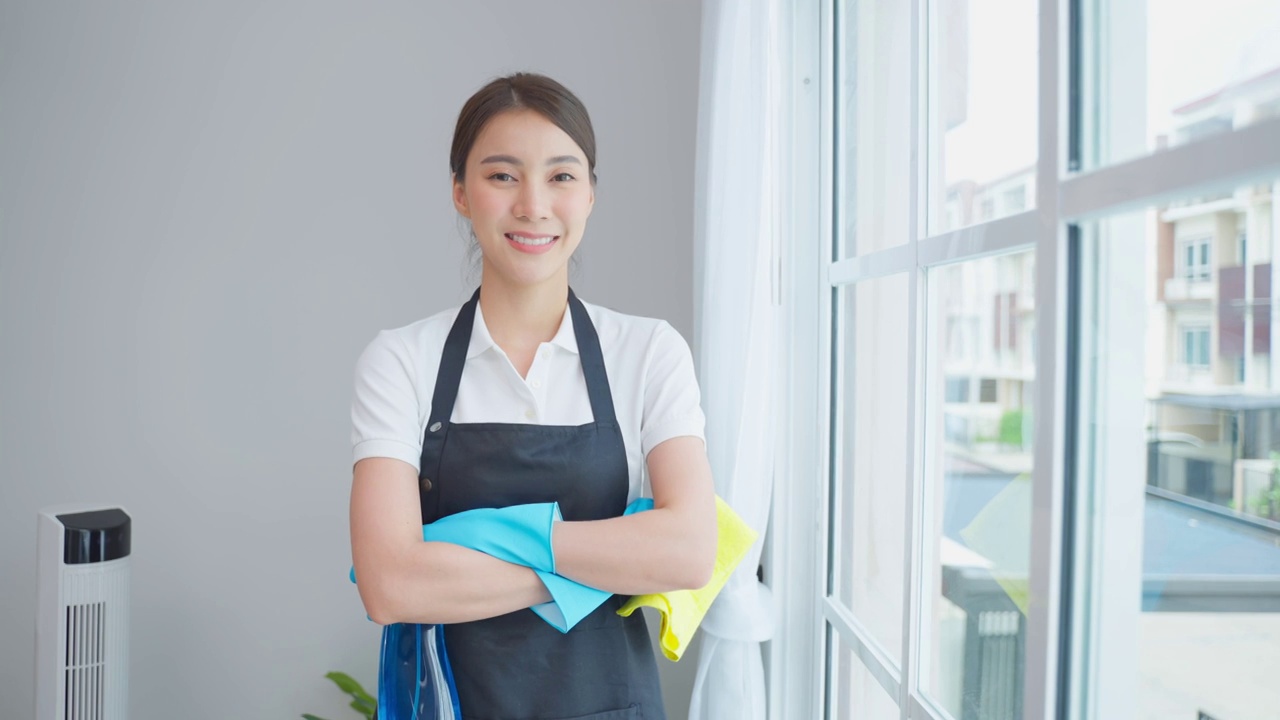 亚洲年轻清洁服务女工在房子工作的肖像。美丽的女孩主妇管家清洁工交叉手臂微笑，在做家务或家务后看着相机。视频素材