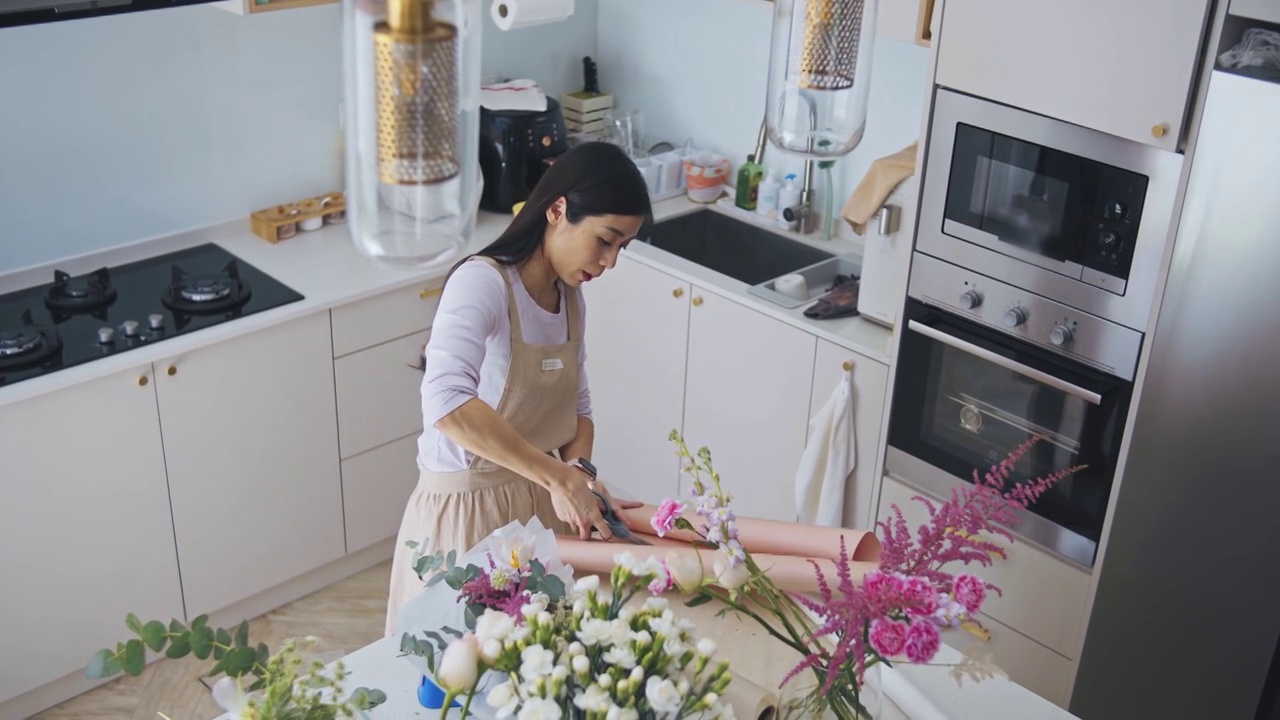 亚洲华人女性花商，小企业主，在厨房为花束剪包装纸，在家里工作，日常运作一个小生意视频素材画面1