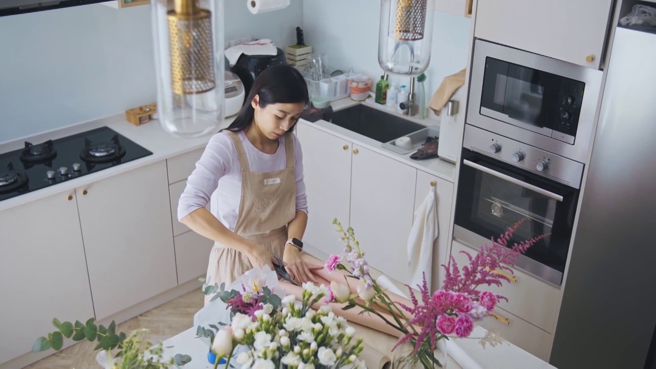 亚洲华人女性花商，小企业主，在厨房为花束剪包装纸，在家里工作，日常运作一个小生意视频素材画面2