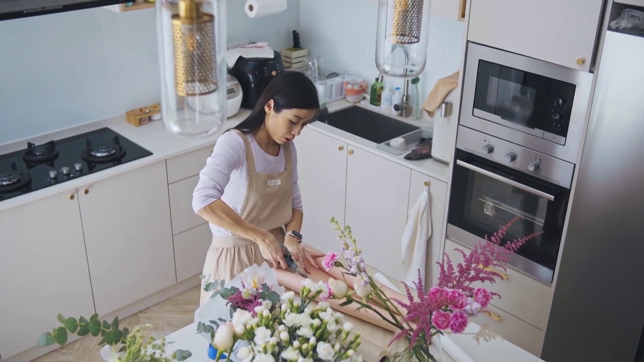 亚洲华人女性花商，小企业主，在厨房为花束剪包装纸，在家里工作，日常运作一个小生意视频素材画面3