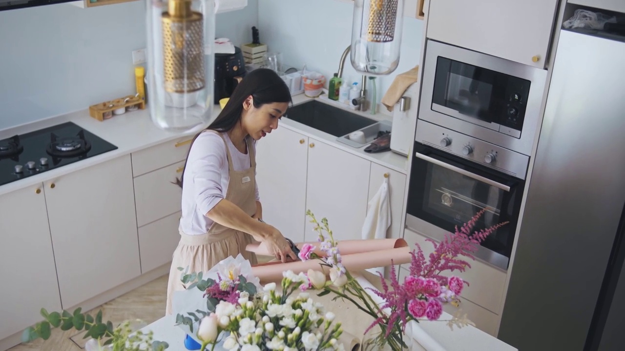 亚洲华人女性花商，小企业主，在厨房为花束剪包装纸，在家里工作，日常运作一个小生意视频素材画面4