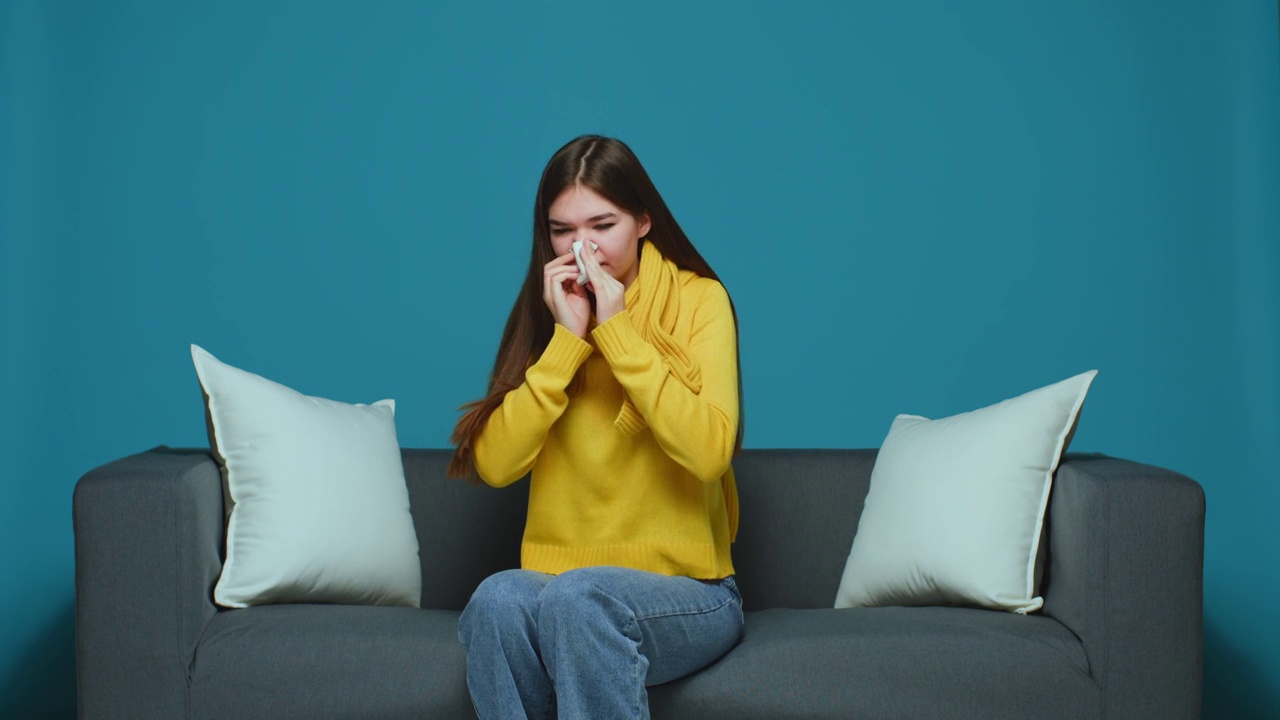 生病过敏的年轻女孩打喷嚏，擤鼻涕，患流感或过敏症状坐在沙发上视频素材