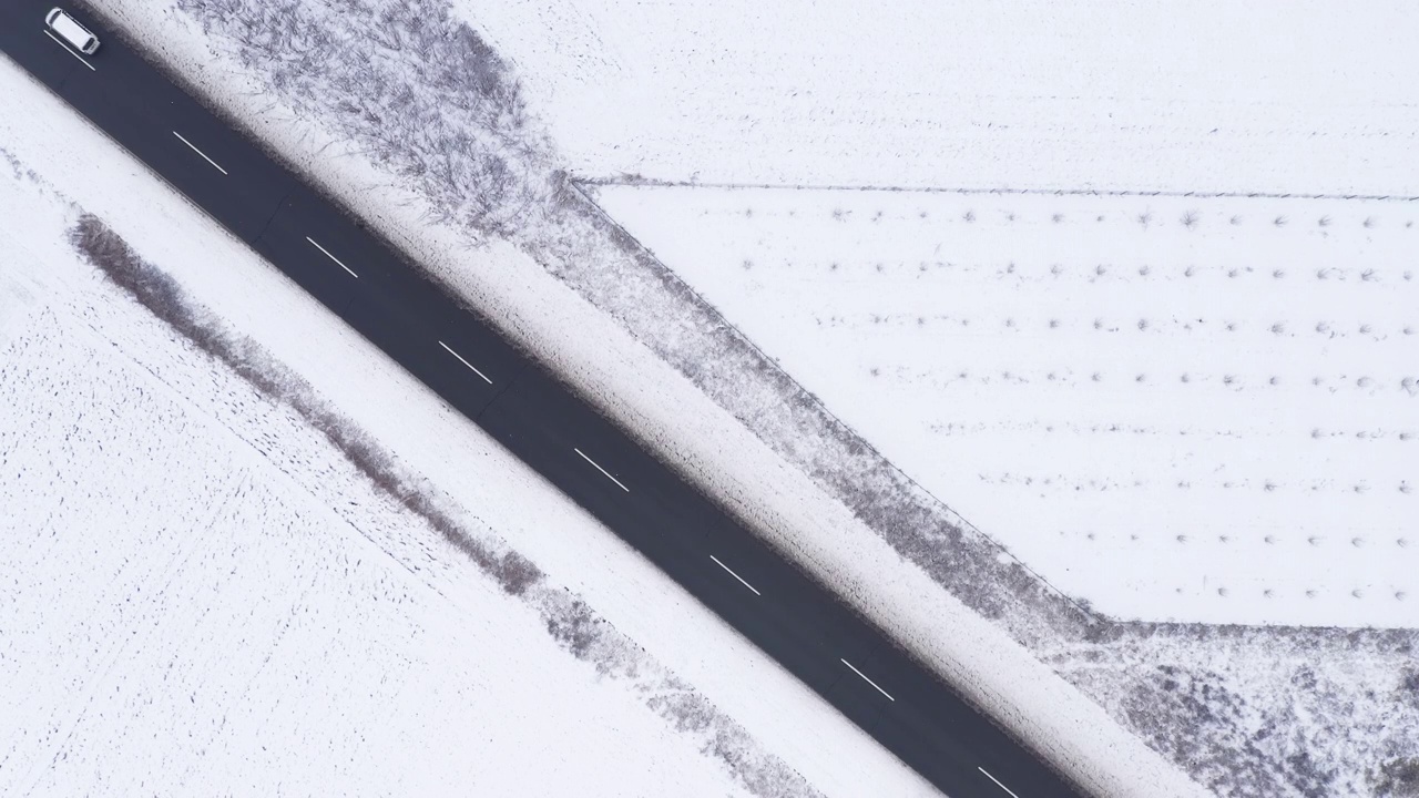 鸟瞰图中的白色汽车在道路上通过冰冻的乡村景观覆盖的雪视频素材