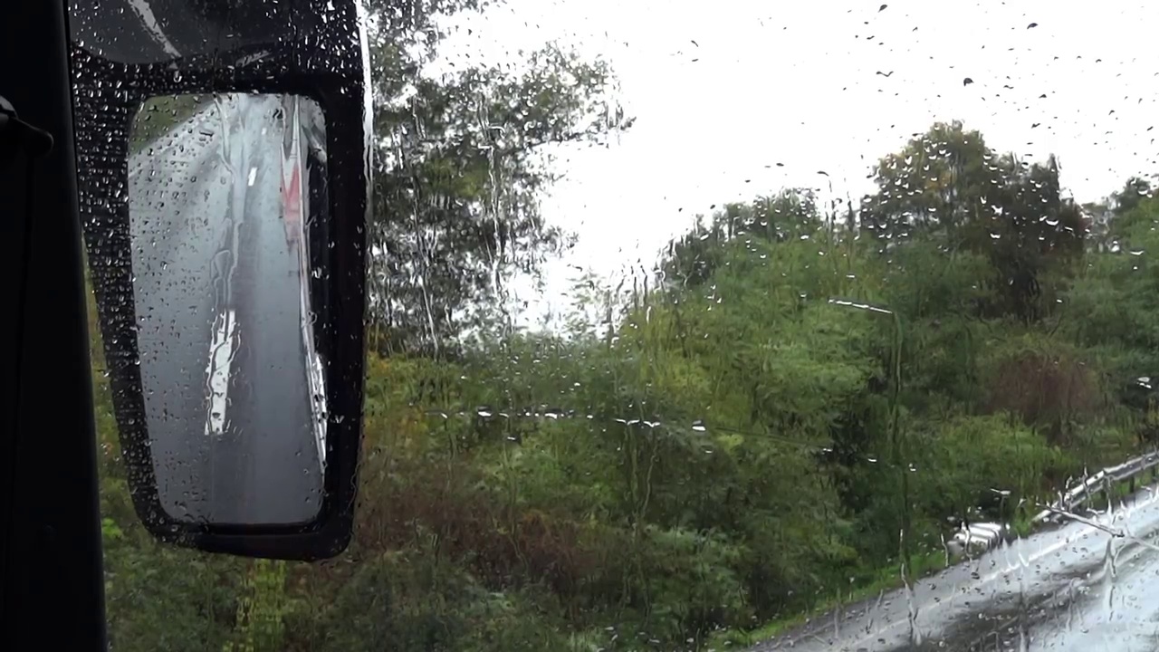 从一辆公共汽车的后视镜里可以看到被雨水浸透的道路上的车流视频素材