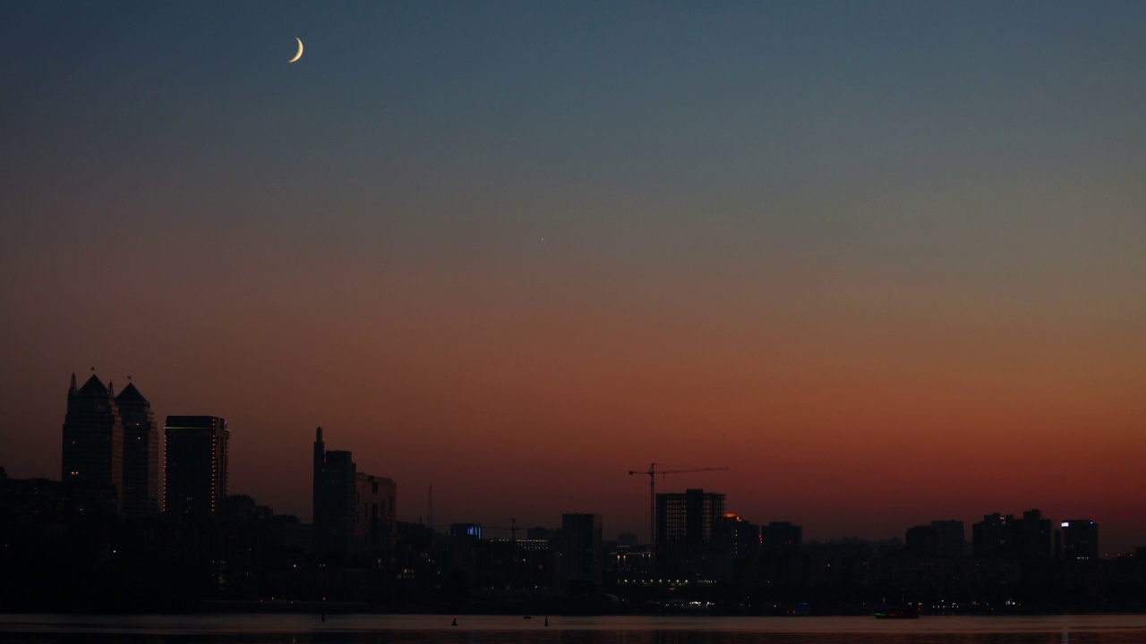 夜晚，河岸上的城市建筑上有半月形的月亮视频素材