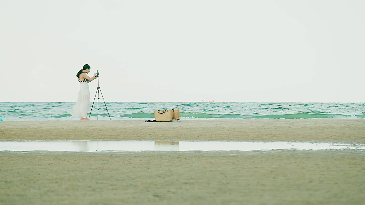 柔焦点幸福年轻女子拍摄照片与三脚架在沙滩热带海滩对水浪海背景在泰国夏季视频素材