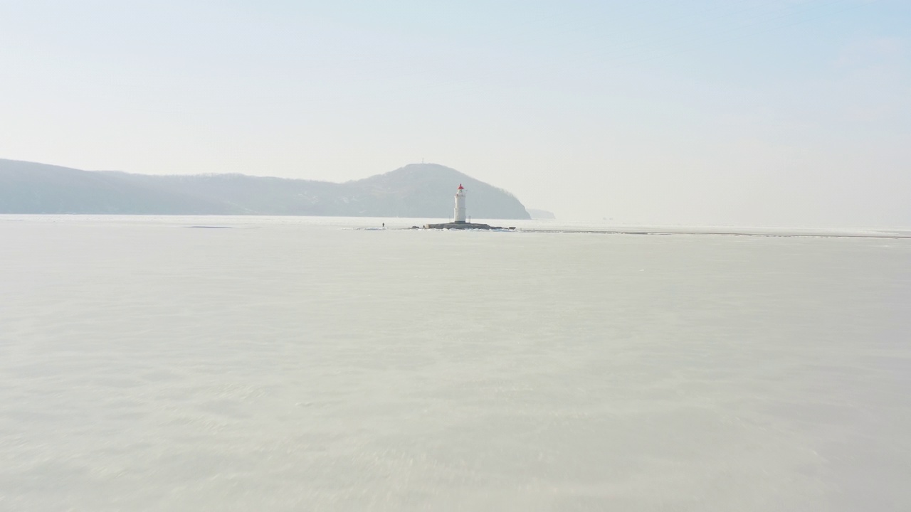 在冰冻的海面上飞行，黎明时分的托卡列夫斯基灯塔的无人机景象视频素材