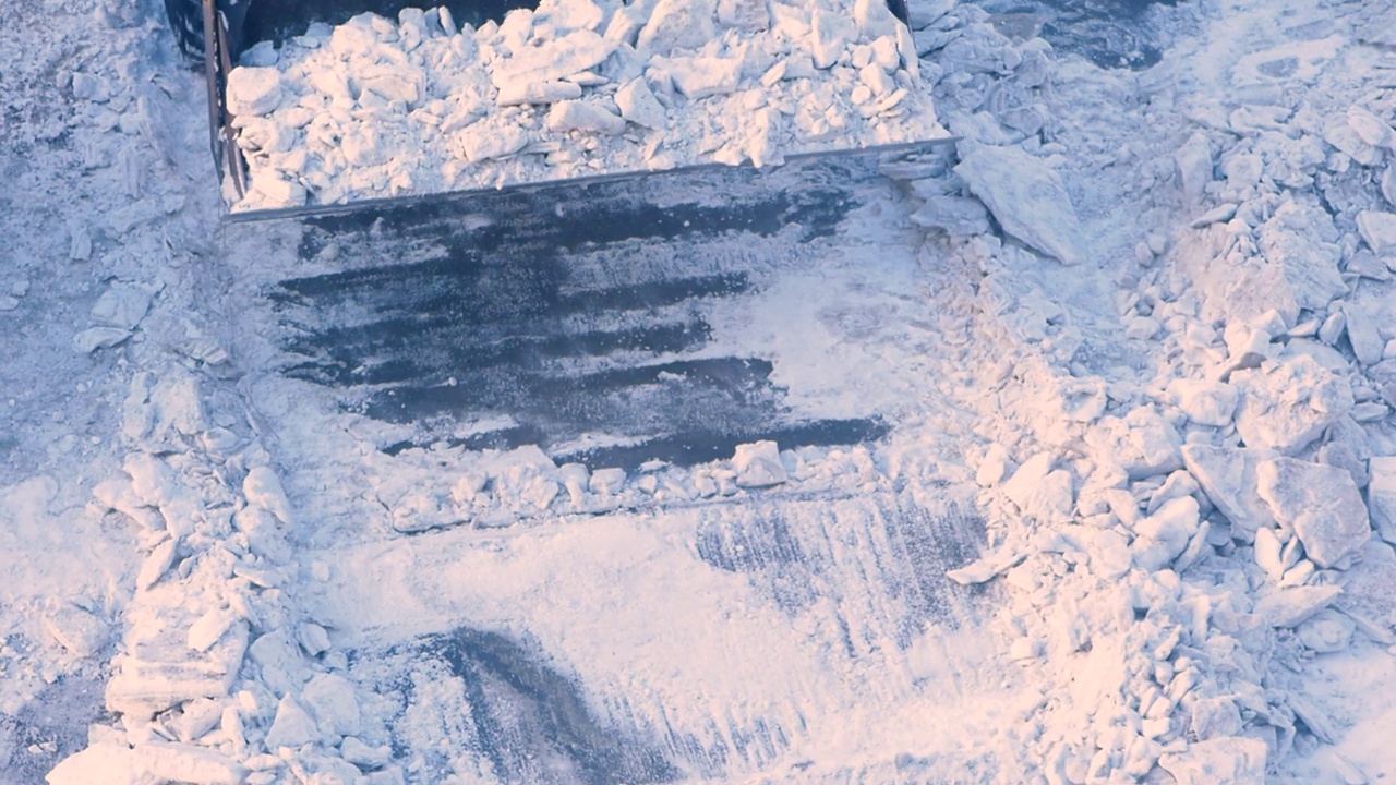 一辆带着铲斗的推土机正在清除城市道路上的冰雪。清理积雪对街道的影响。用扫雪机清理道路。拖拉机清理积雪的工作视频素材