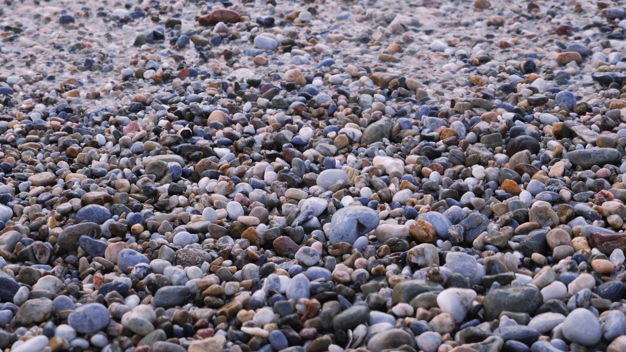 沙滩上的鹅卵石，靠近点。海浪到达卵石滩，形成白色泡沫纹理。卵石海滩视频素材