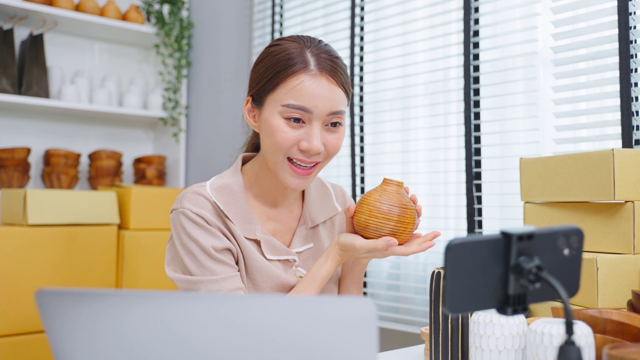 亚洲美女在家在线直播卖花瓶产品。年轻漂亮的女孩用笔记本电脑向顾客展示商品并呈现细节。远程购买和购买购物概念视频素材