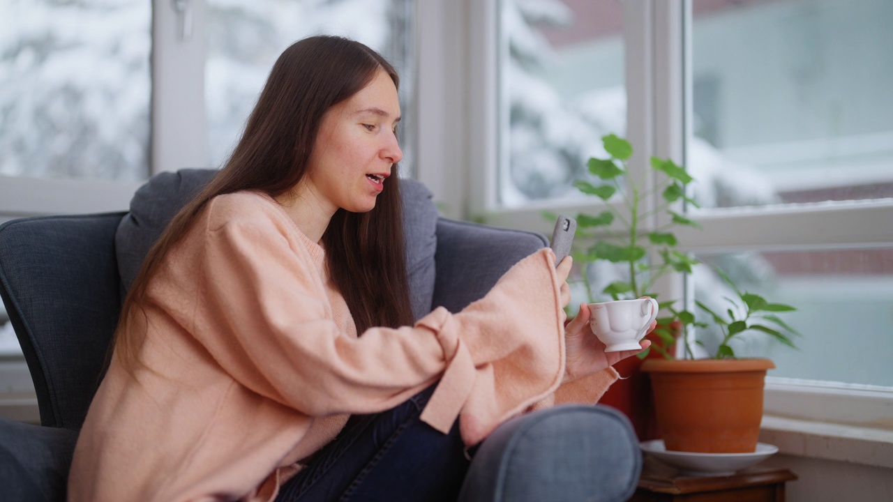 美丽的女人坐在沙发上用智能手机的肖像视频素材