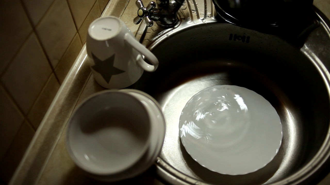 厨房用具、盘子和杯子在水槽里，水从水龙头滴落到盘子里。视频素材