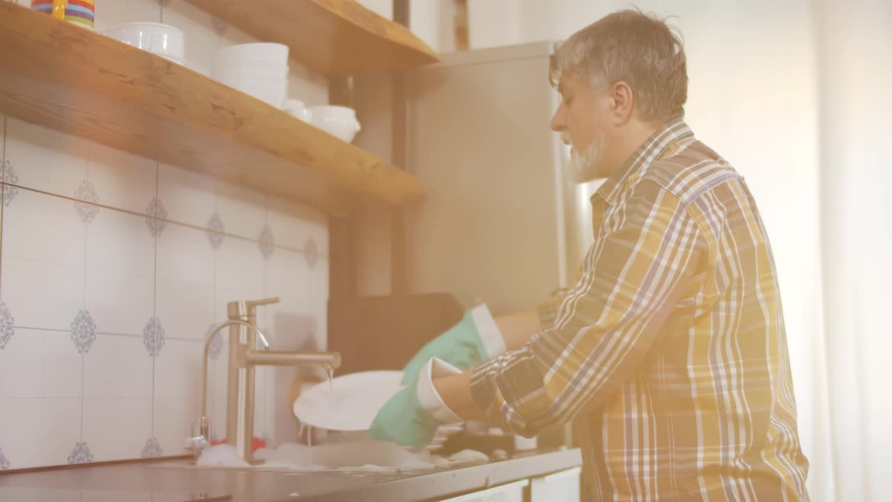 留着胡子的中年男子戴着手套在家洗碗视频素材