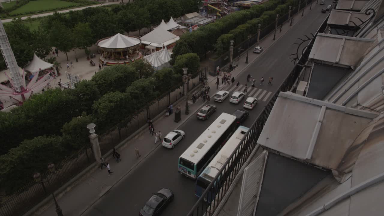 高角度下的汽车行驶在城市街道附近的林荫大道。狂欢节游乐设施和游戏部分可见。可能是嘉年华，集市，或者马戏团。视频素材