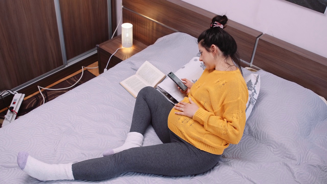 孕妇一边在卧室看书一边上网。视频素材画面3