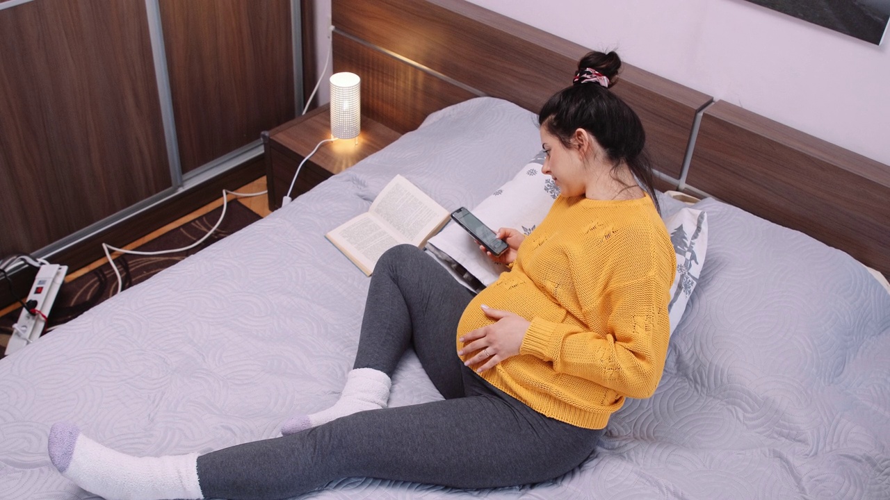 孕妇一边在卧室看书一边上网。视频素材画面4