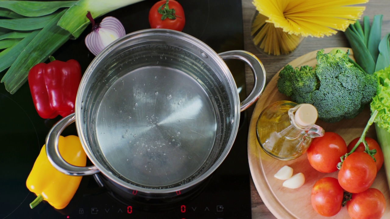 在不锈钢锅中烧开水，准备烹饪食物。新鲜蔬菜的背景。前视图。视频素材